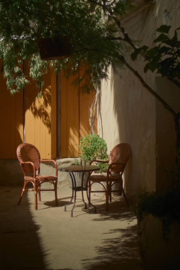 Rustig terras met gele luiken, twee lege rieten stoelen in de ochtendzon